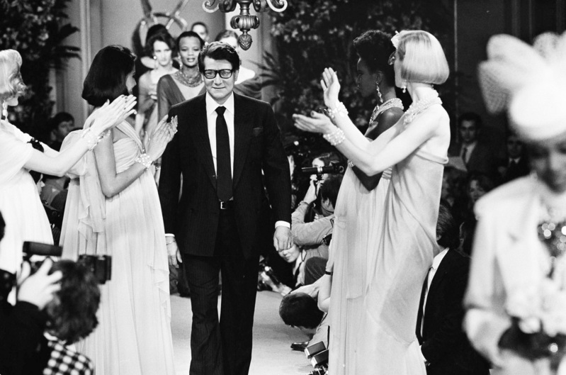 **  FILE ** In this Jan. 25, 1984 file photo, French designer Yves Saint Laurent, center, surrounded by some of his models acknowledges applause from the audience following the presentation of the Spring collection in Paris. Yves Saint Laurent, who reworked the rules of fashion by putting women into elegant pantsuits that came to define how modern women dressed, died Sunday evening June 1, 2008. He was 71. (AP Photo/Jacques Langevin, File)